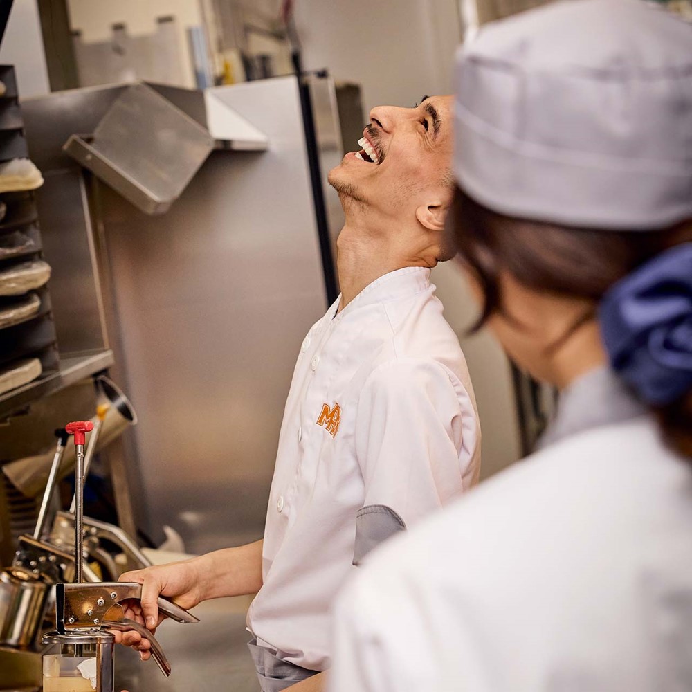 <p>Restaurangpersonal st&aring;r vid en av stationerna i k&ouml;ket och skrattar.</p>